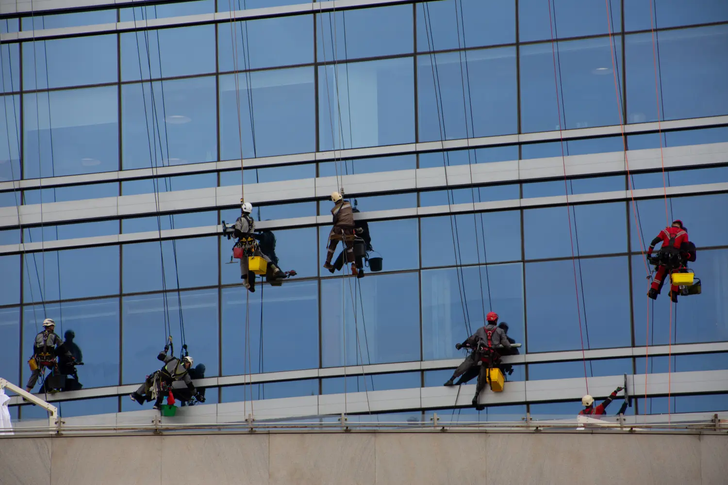 Gruppe von Bergsteigern reinigt das Glas eines Wolkenkratzers auf speziellen Halterungen mit Versicherung